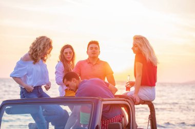 Grup günbatımı sırasında sahilde Cabrio araba içinde eğleniyor içecekler genç insan