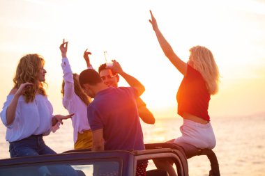 Grup günbatımı sırasında sahilde Cabrio araba içinde eğleniyor içecekler genç insan