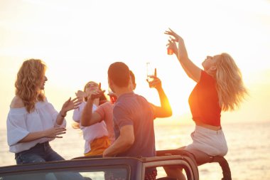 Grup günbatımı sırasında Plajı'nda Cabrio araba içinde eğleniyor içecekler genç insan