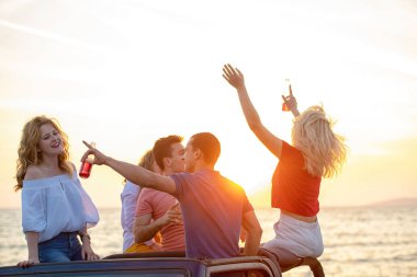 Grup günbatımı sırasında Plajı'nda Cabrio araba içinde eğleniyor içecekler genç insan