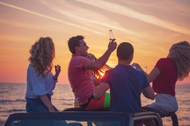 Grup günbatımı sırasında sahilde Cabrio araba içinde eğleniyor içecekler genç insan