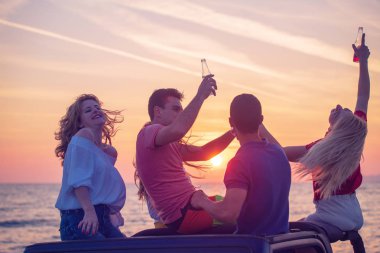 Grup günbatımı sırasında Plajı'nda Cabrio araba içinde eğleniyor içecekler genç insan