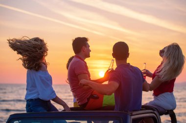 Grup günbatımı sırasında Plajı'nda Cabrio araba içinde eğleniyor içecekler genç insan