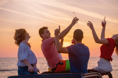Grup günbatımı sırasında Plajı'nda Cabrio araba içinde eğleniyor içecekler genç insan