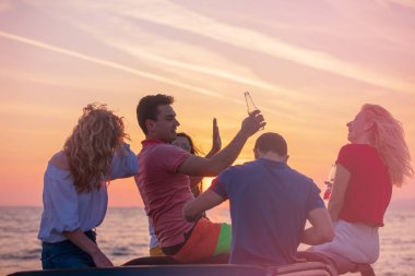 Grup günbatımı sırasında sahilde Cabrio araba içinde eğleniyor içecekler genç insan