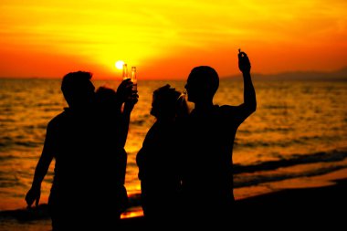 Plaj partisi günbatımı sırasında genç insan siluetleri