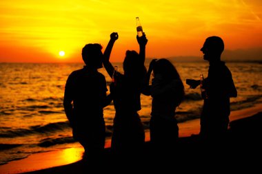 Plaj partisi günbatımı sırasında genç insan siluetleri
