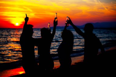Plaj partisi günbatımı sırasında genç insan siluetleri