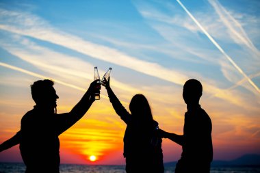 Plaj partisi günbatımı sırasında genç insan siluetleri