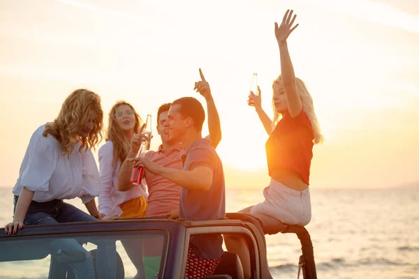 小组的年轻人与饮料有乐趣在敞篷车在海滩在日落期间 — 图库照片