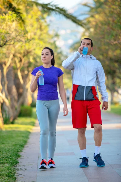 スポーティな若者とスポーツ ウエア ジョギング後水を飲む女 — ストック写真