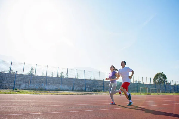年轻的运动情侣在阳光明媚的日子在体育场跑道上慢跑 — 图库照片