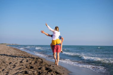  Sahilde sırtında kadın taşıyan bir adam.
