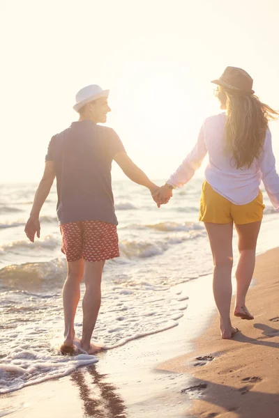 carefree man and woman walking at sea shore, back view