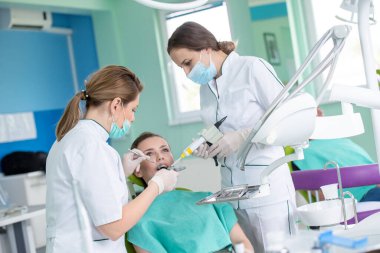 Kadın dişçiler ve dişçi muayenehanesindeki genç bayan hasta.  