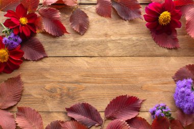 Kırmızı sonbahar yaprakları ve çiçeklerden yapılmış bir çerçeve. Ahşap arka plan. Kopyalama alanı.