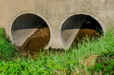 Küçük bir nehrin aktığı iki yuvarlak boru. Bu borular yolun altından geçiyor..