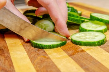 Kadın eli, ahşap bir tabakta salatalıkları yakın mesafeden bıçakla keser.