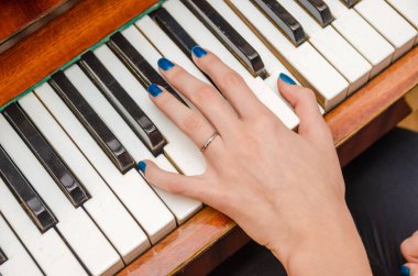 Mavi tırnak cilası olan genç bir kadının eli piyano çalıyor.