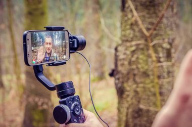 Bir cep telefonunun yakın çekimi ve orman yolunda arka plandaki bir adamın elinde titreşim. Blog yazma konsepti, telefonda çekim..