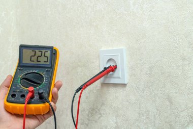 Elektrikçi dijital çokölçer kullanarak prizin voltajını kontrol eder.