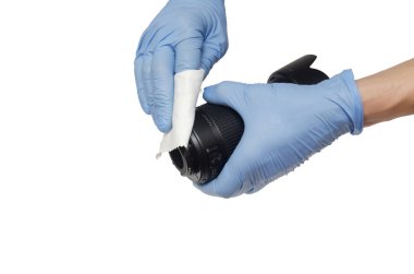 Beyaz arka planda mavi eldivenli eller fotoğraf lensini siliyor.