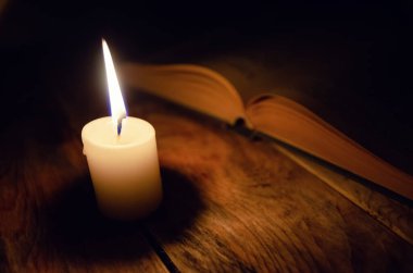 Tahta bir masanın üzerinde, karanlıkta yanan bir mum ve bir kitap. Bilgi, din, sihir kavramı