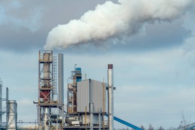 Çevre kirliliği. Bitkinin endüstriyel borusundan yükselen kalın gri-beyaz duman mavi-gri gökyüzüne karşı