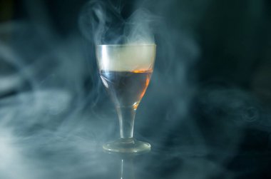 Siyah arka plandaki dumanın içinde bir bardak konyak.