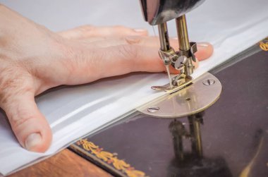 Eski bir dikiş makinesine dikiş diken bir kadının elleri.