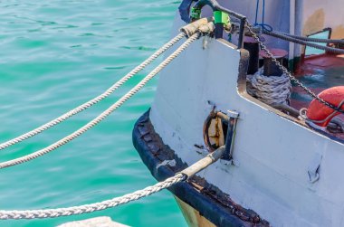 Beyaz iplerle kıyı parçaları. Rıhtımda demirleme halatları olan çelik bir kazığın yakın görüntüsü. İskelede diz çökmüş yaşlı.
