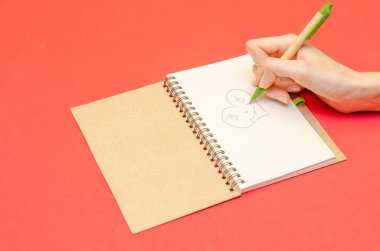 Kırmızı arka plana not defterine kalp çizen bir kızın eli. Sevgililer Günü kavramı, tatil