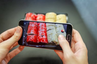 Bir kız telefonda kırmızı ve beyaz suşileri farklı açılardan çekiyor. Fotoğraf kapanışı.