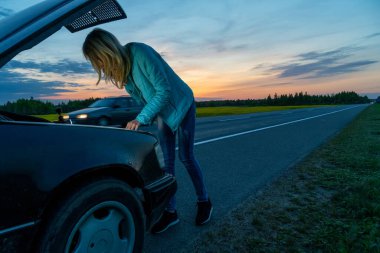 Güzel, ince sarışın kız telefonda konuşuyor ve arabanın kaputunun altına bakıyor. Sarışın kız, akşam üstü gün batımında arabayı bozdu. Yolun ortasında, yardıma ihtiyacım var..