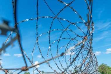 Mavi gökyüzüne karşı çitin etrafına sarılmış dikenli teller.