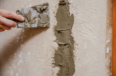 Duvarda içinde elektrik kabloları olan teknik bir delik. Spatula ve çimento karışımlı usta deliği kapatıyor, güvenlik.