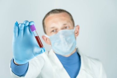 Tıbbi önlüklü, maskeli ve eldivenli bir erkek doktor, üzerinde kan olan bir test tüpü tutuyor. Tıbbi test kavramı