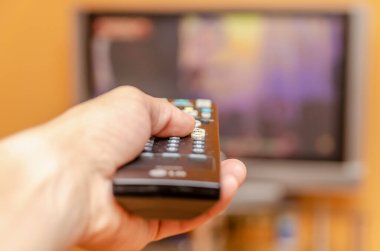 Adamın eli televizyon kumandasını tutuyor, düz ekran televizyonu gösterirken düğmeye basıyor..