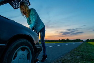 Güzel, ince sarışın kız telefonda konuşuyor ve arabanın kaputunun altına bakıyor. Kız akşamüstü arabayı bozacak, yardıma ihtiyacı var..