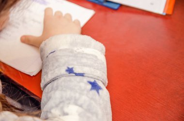 Güzel örgülü bir kız masada bir okul konusu üzerinde ödev yapıyor. Fotoğraf arkada, boşluğu kopyalamak için boşluk var