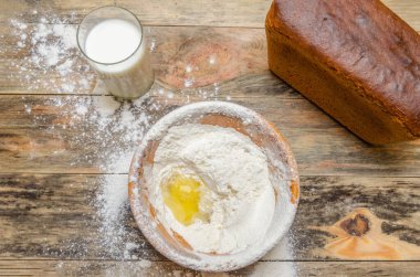 Taze ekmek tuğlası masaya yakın çekim. Sırada bir kase un ve yumurta var, bir bardak süt. tepeden görünüm