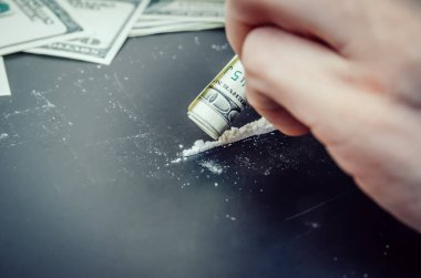 Erkek eller siyah bir arka planda bir dolar üzerinden uyuşturucu kokluyor.