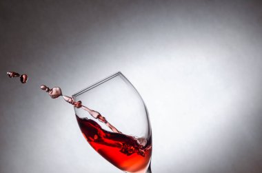 Sıçrayan bardaklar, beyaz arka planda kırmızı şarap damlaları. Dondurucu sıvılar hareket halinde. Fotokopi alanı olan bir bardak kırmızı şarap.