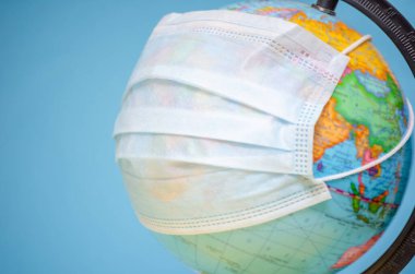 Tıbbi maskeli bir küre mavi arka planda, uzayın bir kopyasıyla birlikte. Koronavirüs konsepti, bulaşıcı hastalıklar