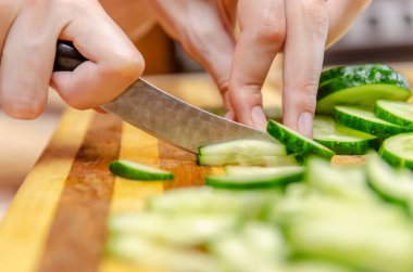 Kadın eli, ahşap bir tahtanın parmaklıklarında bıçakla salatalıkları kesiyor.
