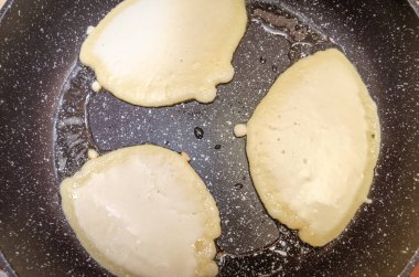 Siyah bir tavada üç krep kızartılıyor. Kahvaltı konsepti.