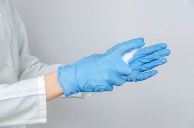 Beyaz önlüklü ve mavi eldivenli doktor ellerini antiseptik spreyle dezenfekte ediyor.