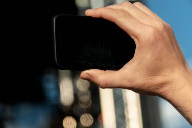 Siyah ekranlı bir akıllı telefonu tutan ve olanları yakından çeken kişi.