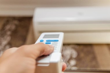 Karanlık bir duvardaki klimayı hedef alan uzaktan kumandayla bir adamın eline yakın çekim.