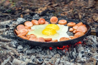 İki yumurta ve sosis ormanda kömürde tavada kızartılır. Doğada kahvaltı, piknik..